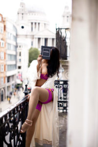 kio jones ebony london escort and travel companion sits cheekily on a balcony in London with the st pauls skyline in the background